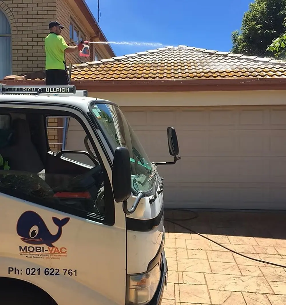 A Mobi-Vac operator treating a Christchurch roof, with the truck parked below